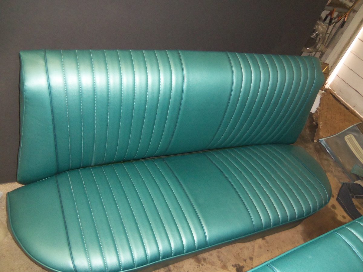 A bench seat recovered in green vinyl with vertical pleats running front to back.
