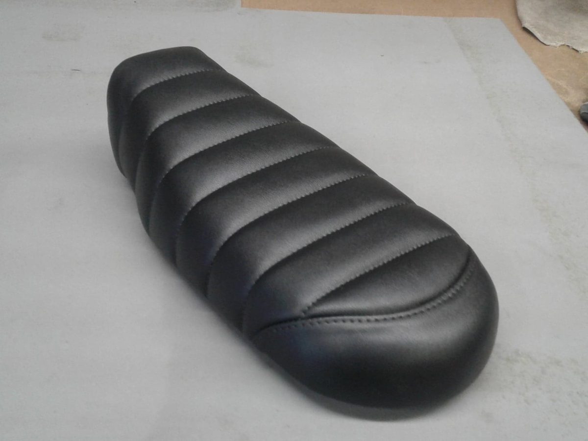 A motorcycle seat recovered in black vinyl with ribbed pleats across the top.