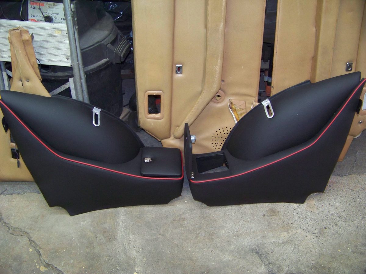 Black door panels with red piping, propped up beside a tan car interior.