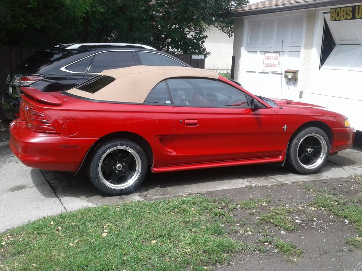 A red convertible with a tan soft top, parked outside the shop.
