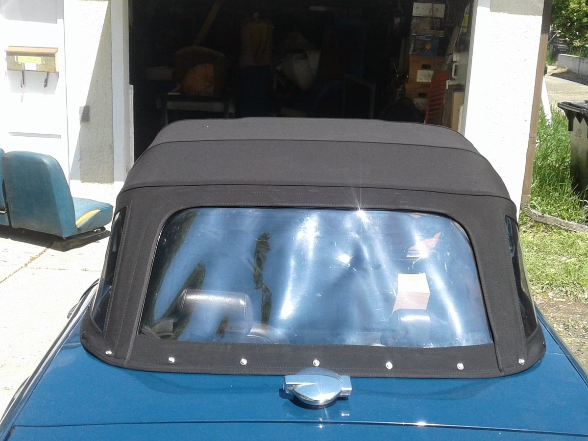 A black convertible soft top fitted to a blue sports car, with a clear rear window.