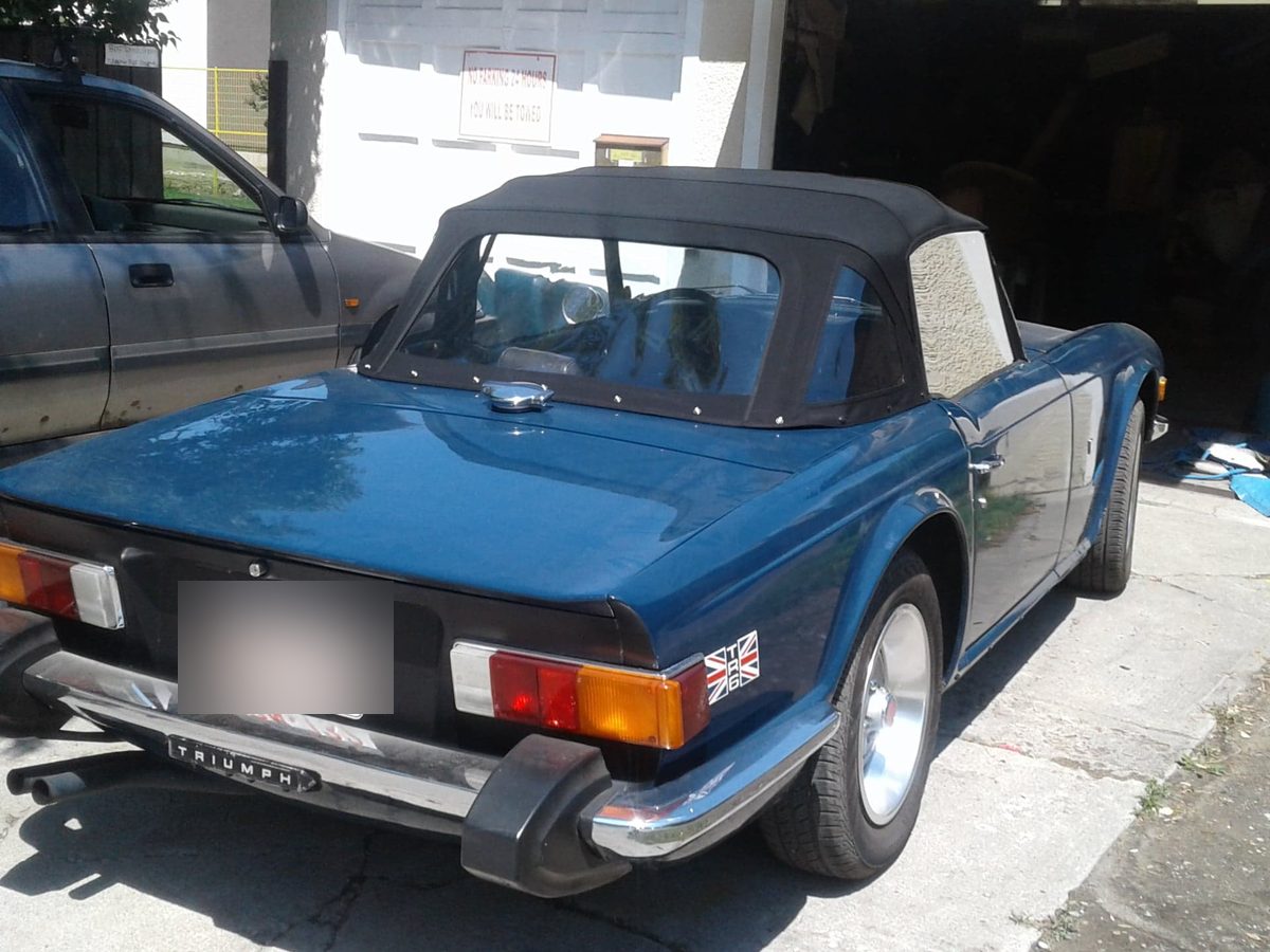 A blue Triumph convertible parked outside the shop with a new black top fitted.