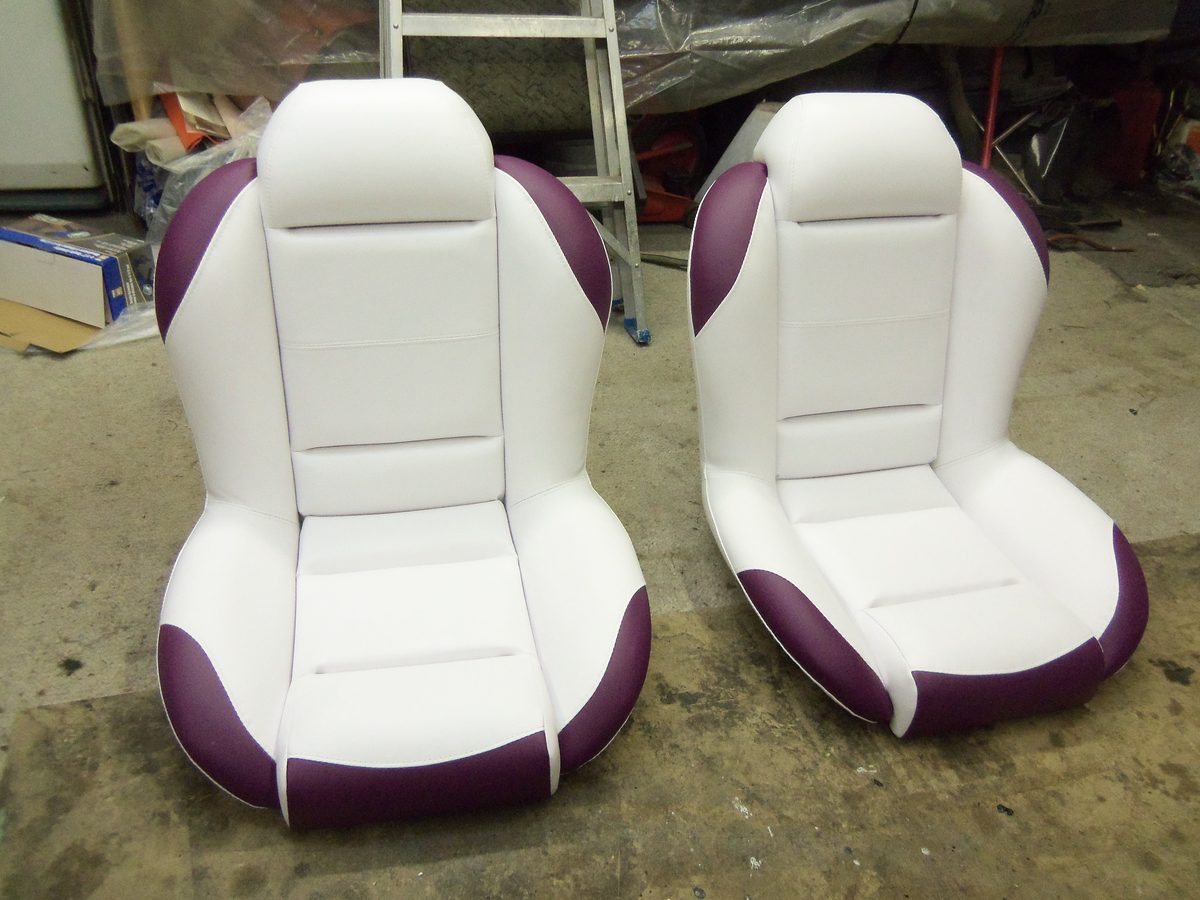 A pair of bucket seats recovered in white vinyl with burgundy side bolsters.